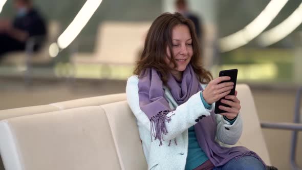 Female Passenger Is Resting in Lounge Area in Airport, Chatting Online By Smartphone