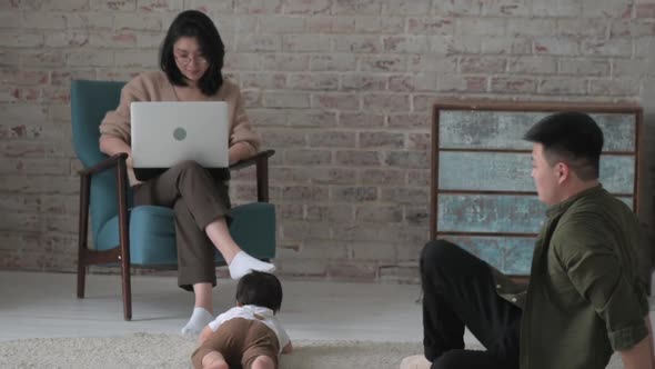 Mother works on laptop inside room while father takes care of his beloved son