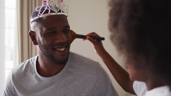 African american father wearing tiara having makeup put on by his daughter