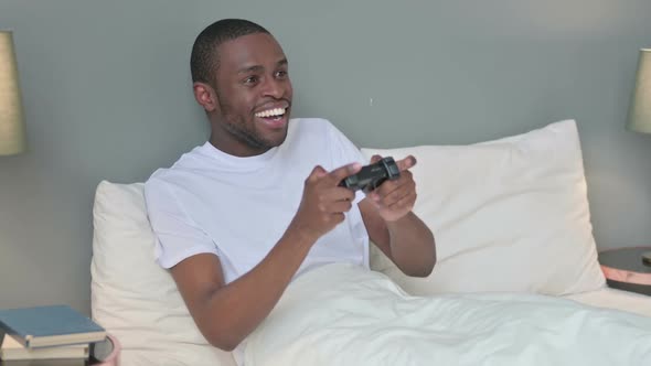 Excited Young African Man Playing Video Game in Bed