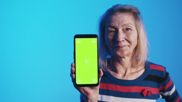 Mature Woman Holding Smartphone with Green Screen and Nodding Head