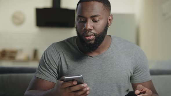 Black Man Holding Phone at Open Kitchen. Concentrated Guy Texting in Smartphone.