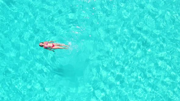 Aerial view of an attractive woman doing backstroke in crystal clear sea alt
