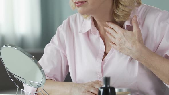 Unsatisfied Woman in Her 50s Looking Into a Hand Mirror, Anti-Age Cosmetics