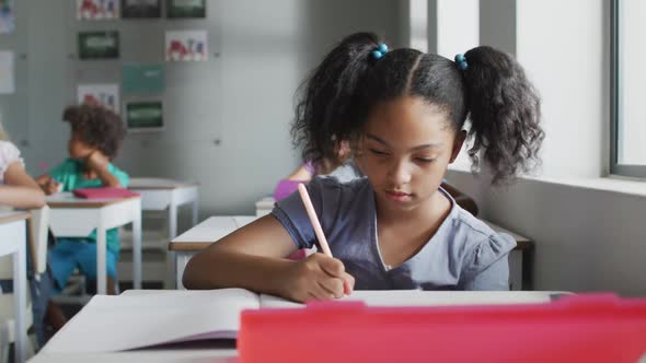 Video of focused biracial girl sitting at desk in classsroom