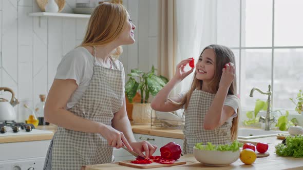 Mature Mother Cuts Red Peppers in Kitchen Cooking Salad with Teenager Girl Daughter Child Takes Two