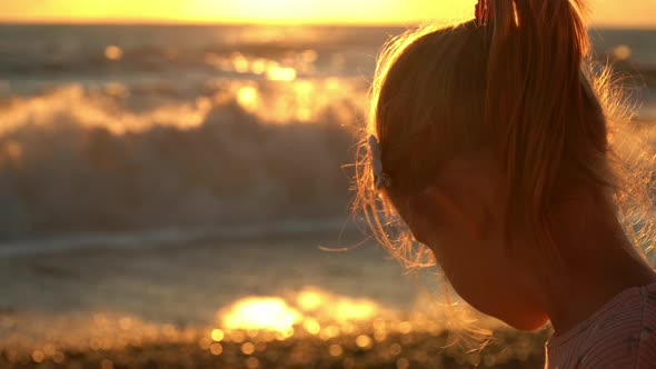 Back View of Girl Sits By Sea and Looks at Waves and Summer Sunset Holiday