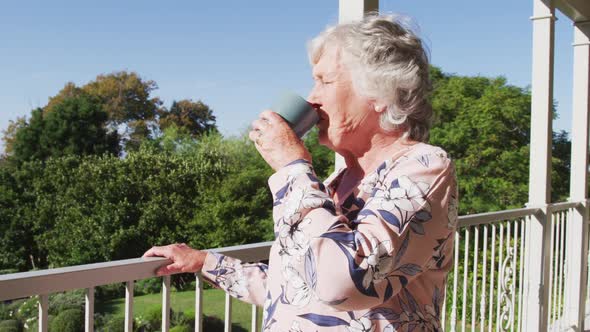 Thoughtful caucasian senior woman drinking coffee while standing in the balcony at home