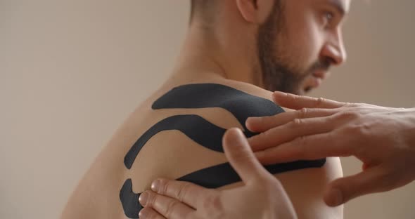 Kinesiologist Sticks Tapes to the Shoulder of Man Recovery of an Athlete After Injury Kinesiotherapy