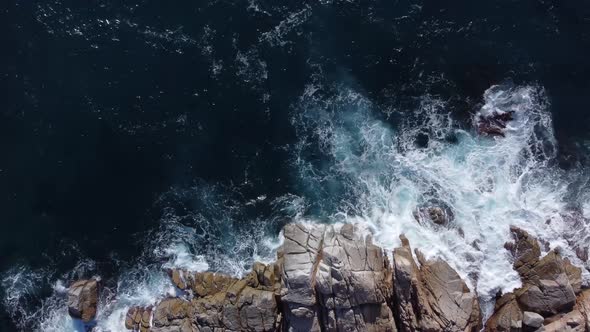 Foamy waves of sea splashing on rocky shore in sunlight