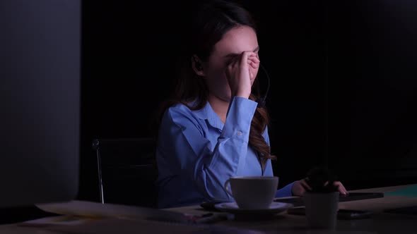 Sleepy Asian woman working late at night, drinking coffee to refresh herself