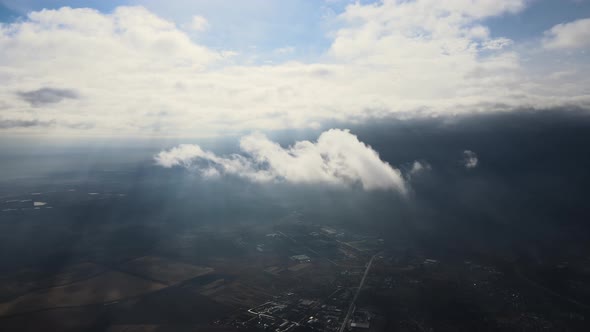 Aerial View From High Altitude of Distant City Covered with Puffy Cumulus Clouds Flying By Before