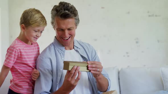 Son giving gift box to father in living room