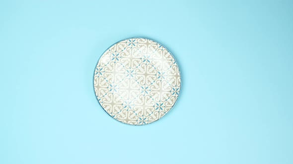 female hands put on a blue background metal fork and knife, next to a round ceramic plate