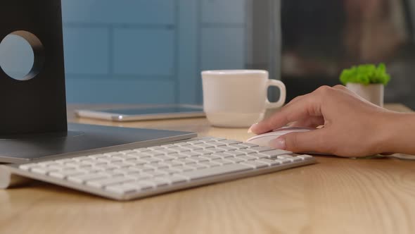 A Woman Controls a Computer Mouse and Typing on a White Keyboard Sitting at an Office Table or at