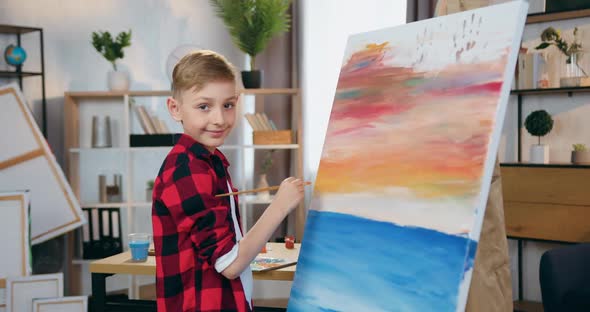 Boy which Standing in Front of Easel with Canvas and Drawing Picture in Home Studio