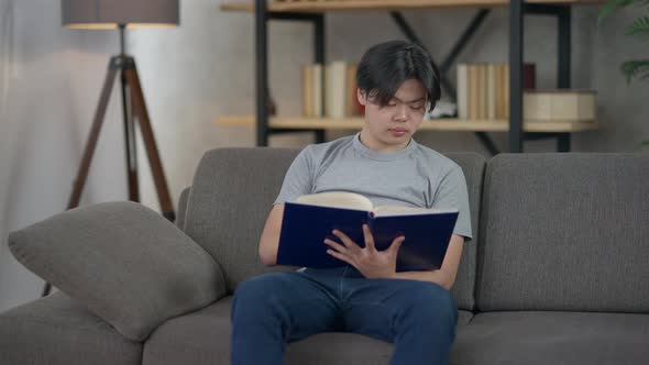 Young Asian Man Sitting on Couch in Living Room Turning Pages of Sketchpad