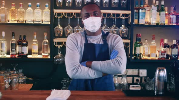 Smiling African Waiter in a Face Mask is Standing Behind the Bar