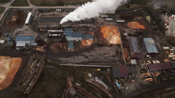 Revealing Shot of Operating Log Sawmill Factory with Large Chimney Emitting Smoke Aerial