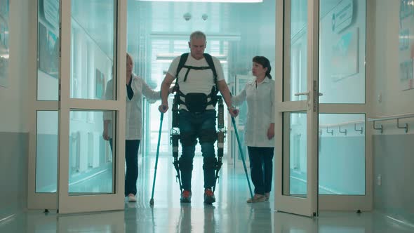 A Man in the Exosuit is Walking with Doctors' Aid