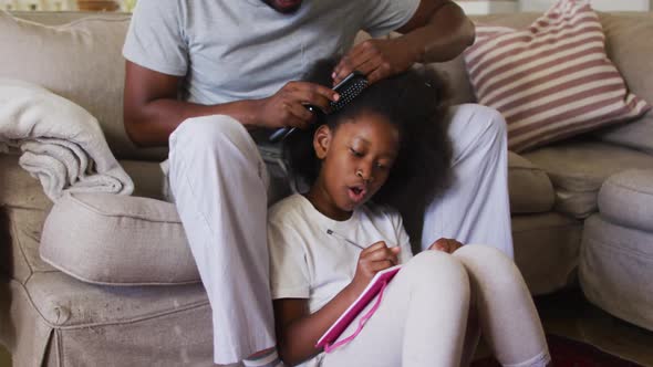 African american father brushing his daughters hair while sitting on the couch at home