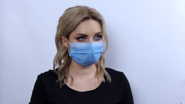 A Beautiful Young Woman with Evening Makeup Smoky Eyes and a Black Dress in a Medical Protective