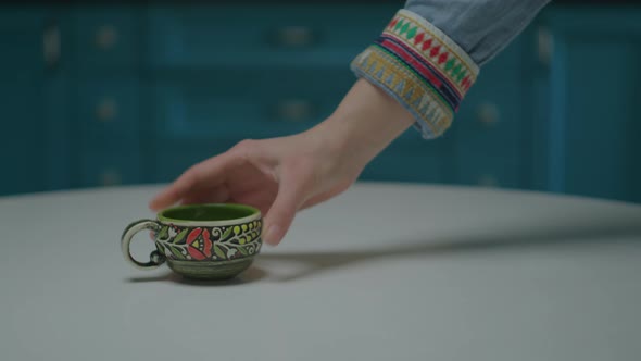 Female Hand Putting Porcelain Coffee Cup and Coffee Pot on the Table in Blue Kitchen Interior