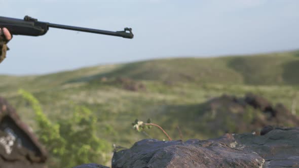 Sniper in Military Equipment Lies Down on Rocks Takes Aim and Pulls Trigger Side View in Outdoor alt