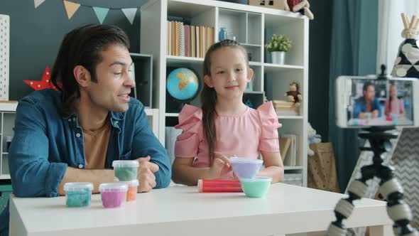 Child Vlogger Recording Video About Play Dough Sitting at Table with Father and Using Smartphone