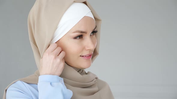 Muslim Woman Wearing Hijab Is Putting Wireless Earphone in Her Ear and Speaking Phone Using Headset