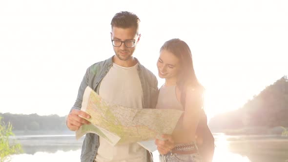 Close up view of Young Couple Hikers in the Wood. Standing by the Lake. Using Tourist Map.