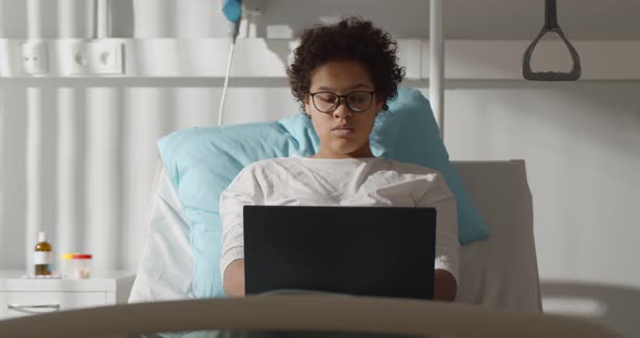 Young African Female Patient Working with Laptop in Bed in Hospital