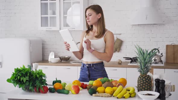 Beautiful woman looking into tablet on the light kitchen background.