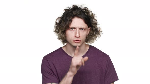 Portrait of Unshaved Curly Guy Posing with Strict Gaze and Asking Keep Quiet Putting Index Finger on