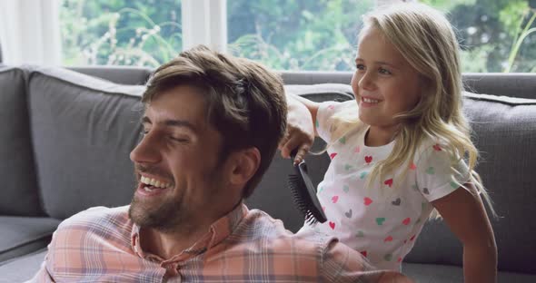 Young daughter combing her fathers hair on sofa at home 4k