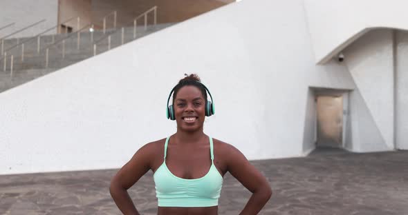 Fit young african woman smiling on camera after sport workout while listening music playlist