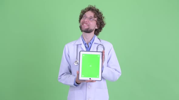 Happy Young Bearded Man Doctor Thinking While Showing Digital Tablet