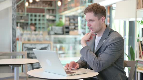 Young Man with Laptop Thinking in Cafe