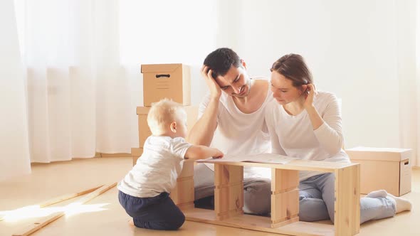 Family Together at Living Room of New Apartment Assembling Furniture, Pile of Moving Boxes on