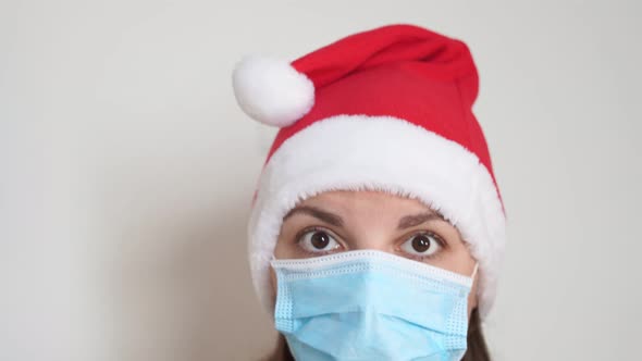 Caucasian Woman Puts on Medical Mask and Santa Christmas Hat. Christmas Celebration on Lockdown