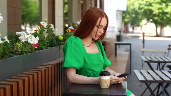 Hand Held Shot Portrait of Happy Young Woman Using Browsing Mobile Phone Sitting at Table with