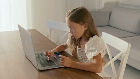 Child Working on Her Laptop at Home and Do Some Operation With a Credit Card