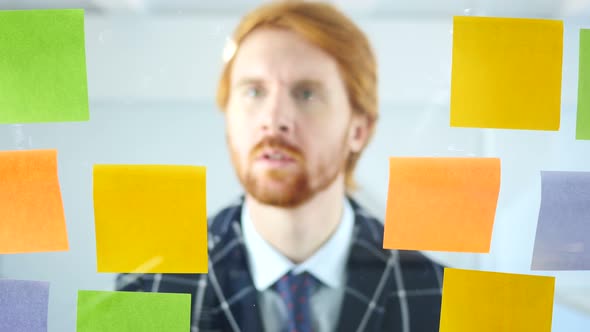 Businessman Working On Sticky Notes Attached on Glass in Office