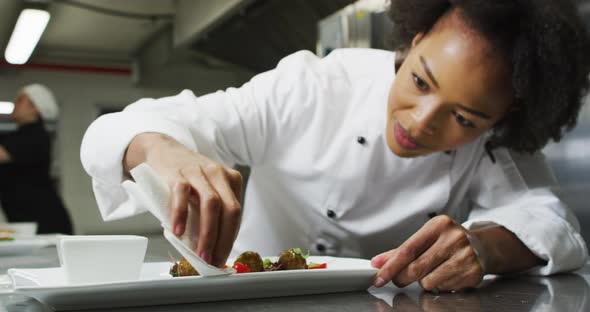 Portrait of african american female chef garnishing dish looking at camera and similing