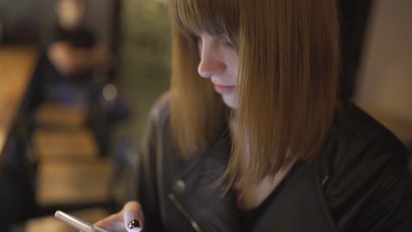 Young Beautiful Redhaired Woman Sitting in Cafe or Bar and Using a Smartphone
