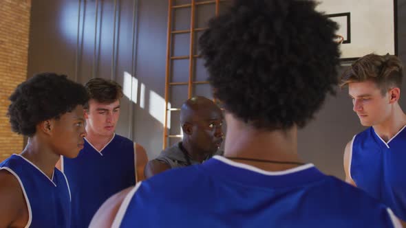 Diverse male basketball team and coach in huddle discussing game tactics