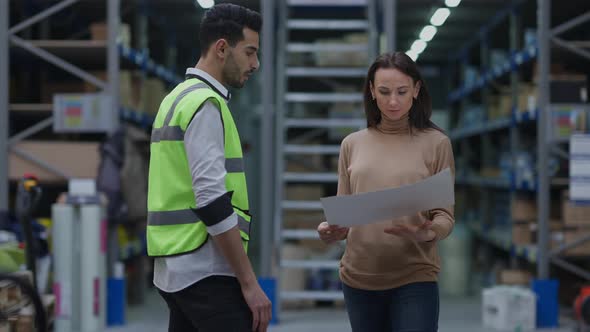 Dissatisfied Angry Caucasian Woman Arguing with Middle Eastern Man in Warehouse Pointing at