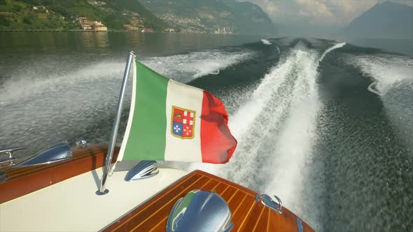 A classic luxury wooden runabout boat with an Italian flag on a lake.