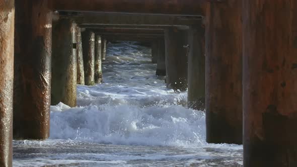 Waves with White Foam Break Against Large Iron and Rusty Columns