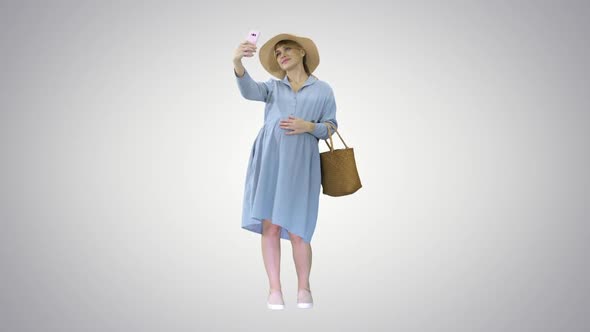 Happy Pregnant Woman in a Hat Using Her Smartphone Doing Selfie on Gradient Background